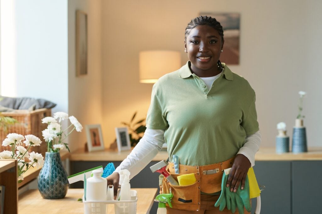 Smiling woman with cleaning supplies. Maid service in Washington DC, ready for home cleaning. Cleaning lady with tools and gloves.