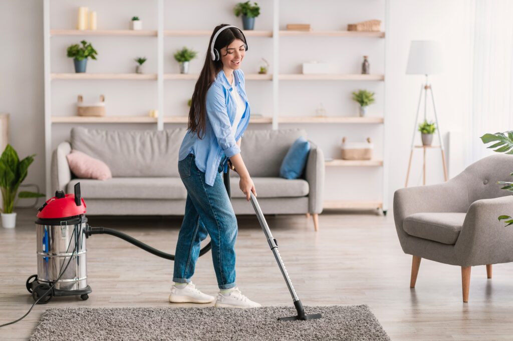 Maid service: Woman in headphones vacuums rug in living room. Professional house cleaning services keep your home tidy and fresh.
