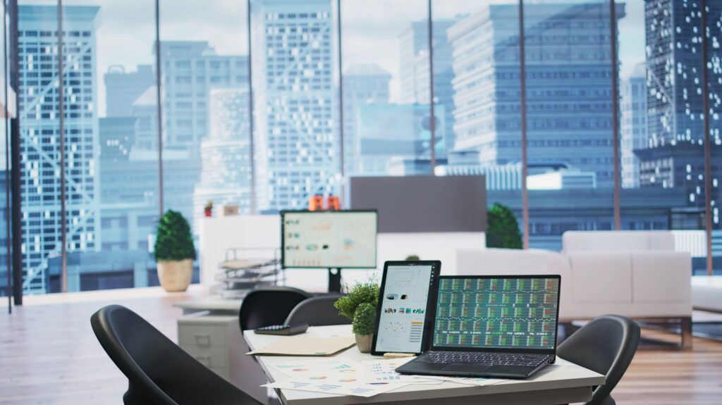 Financial analysis setup in a modern office with a city view. Laptop, tablet, and monitor display charts. Financial services in Washington DC.