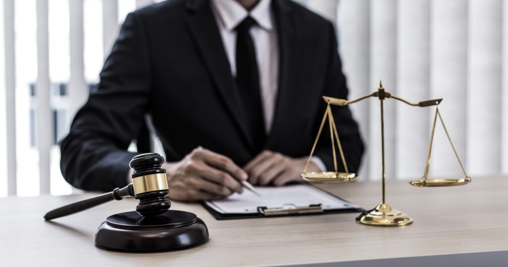 Scales of justice and gavel on a desk with a lawyer in the background. Legal representation and counsel in Washington DC.