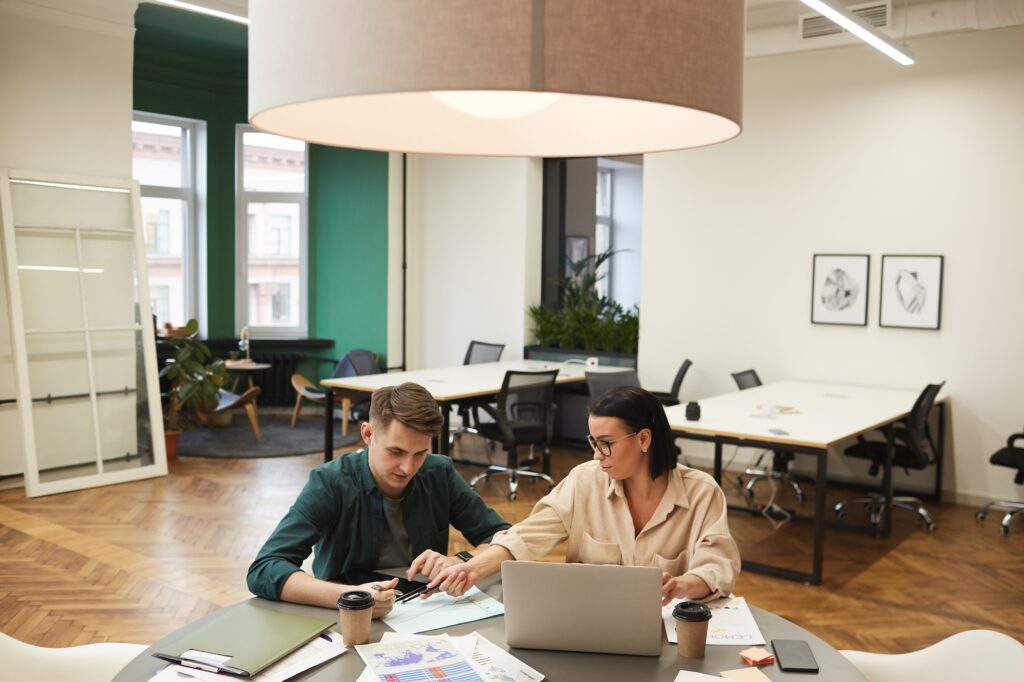 Coworkers collaborating on business strategy in Washington DC. Man and woman reviewing data analysis charts with laptop. Modern office space.