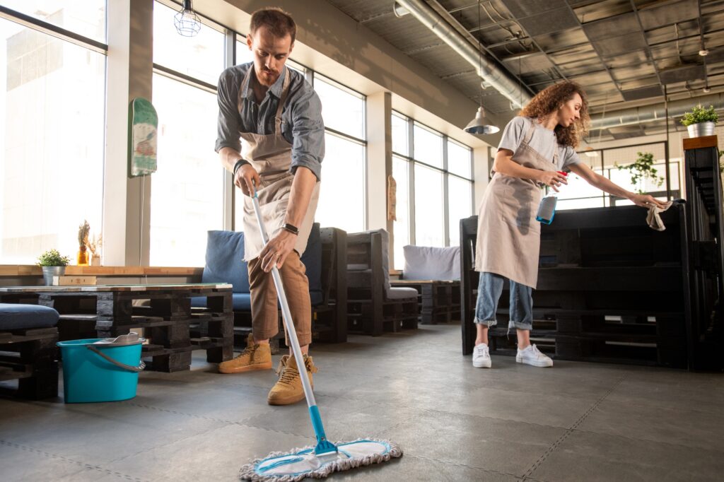 Commercial cleaning services: Two cleaners, one mopping the floor and the other dusting furniture in a commercial space. Professional cleaners in Washington DC.