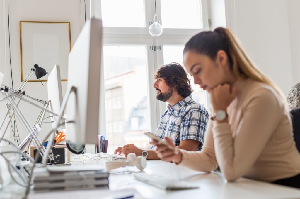 Office workers in Washington DC using computers. Coworkers at desks in a modern office, woman with ponytail and man in plaid shirt.