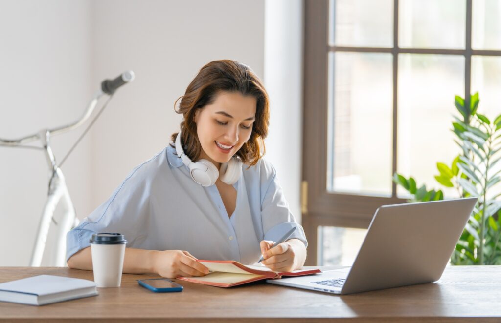 Young woman in Washington DC writing in notebook. Laptop, coffee, and bike. Remote work concept, work from home.