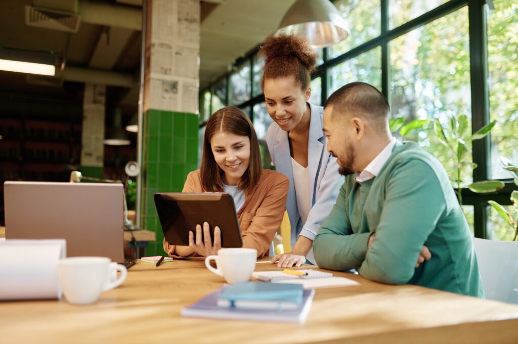 Diverse team collaborating on a tablet at a wooden desk, surrounded by laptops and coffee cups. Business meeting in Washington DC.