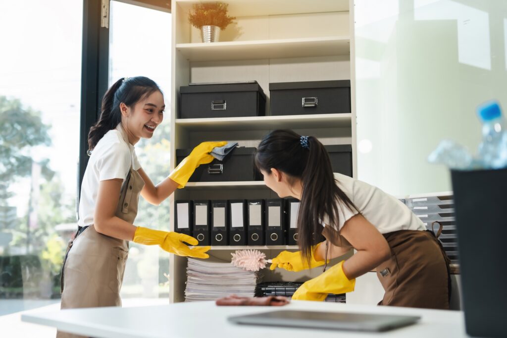 Office cleaning services: Two women in yellow gloves dusting shelves and files in a Washington DC office, smiling and working together to keep the space clean.