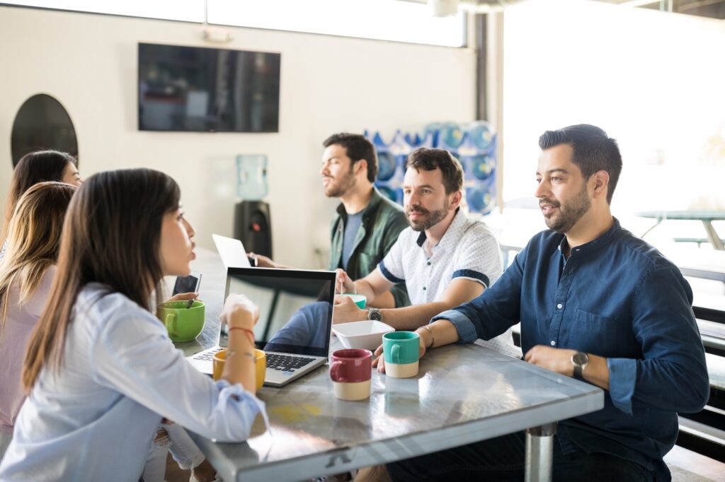 Coworking space in Washington DC with diverse professionals at a table with laptops, having a meeting. Shared office space with natural light.