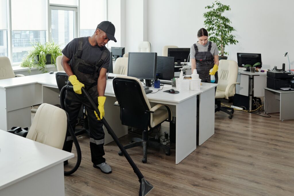 Office cleaning services: Janitors vacuuming and wiping desks in Washington DC. Professional commercial cleaners in an office setting.