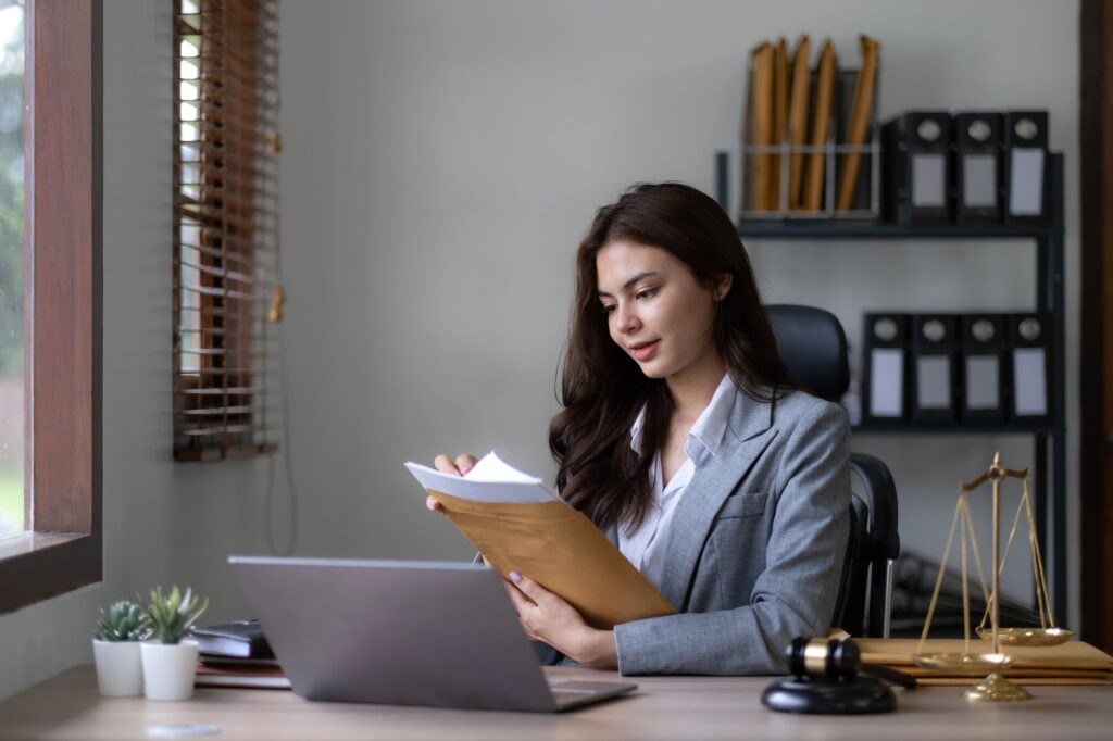 Woman lawyer in Washington DC reviews legal documents at her desk with laptop and gavel. Scales of justice symbolize legal services.
