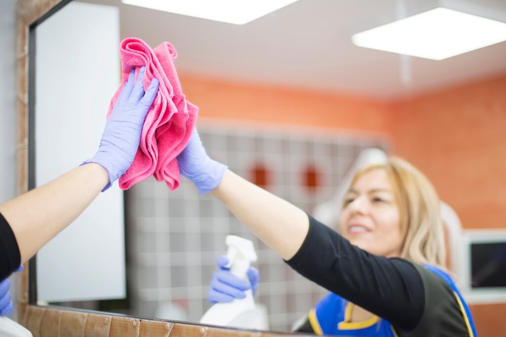 Maid service: Woman in Washington DC cleaning a mirror with a pink cloth and spray bottle. Focus on professional cleaning for sparkling results.