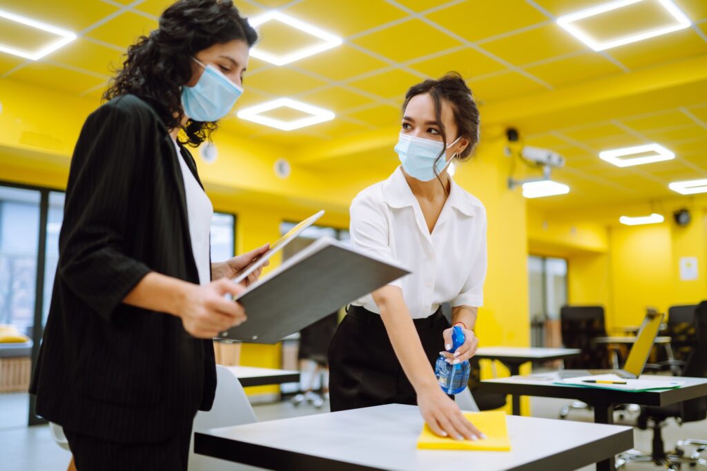Office cleaning service: Women in masks cleaning desks in a bright office. Janitorial services in Washington DC ensure a safe workplace.