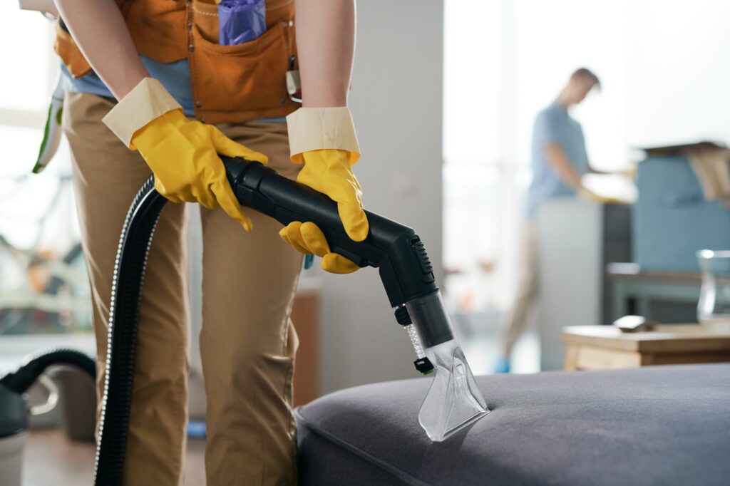 Upholstery cleaning service. Cleaner using a handheld wet vacuum on a couch. Professional upholstery cleaner in Washington DC wearing yellow gloves.