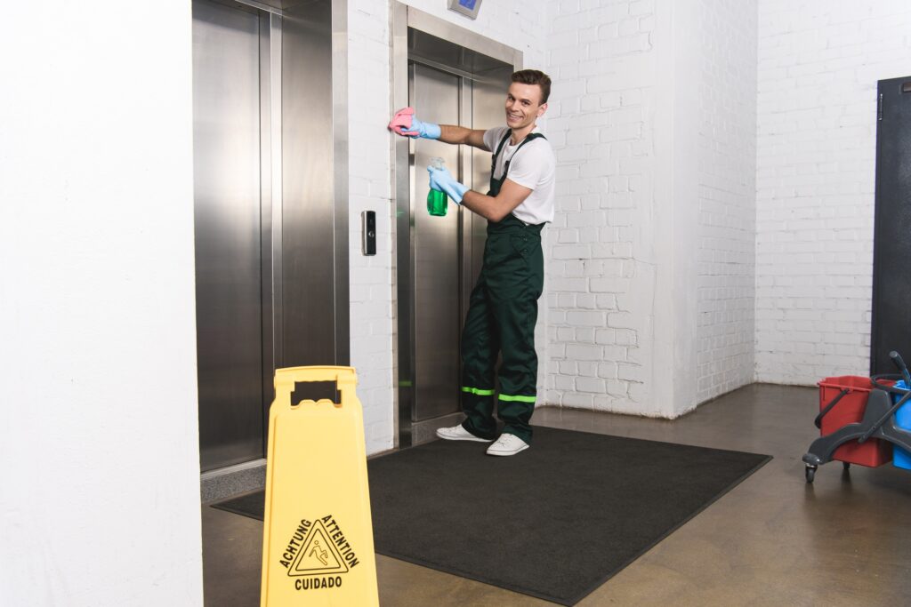 Janitorial service worker cleaning an elevator in Washington DC. Safety sign and cleaning supplies visible. Commercial cleaning services.