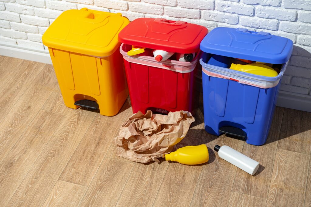 Recycling bins in yellow, red, and blue for sorting waste. Paper bag and plastic bottles on the floor. Waste management in Washington DC.
