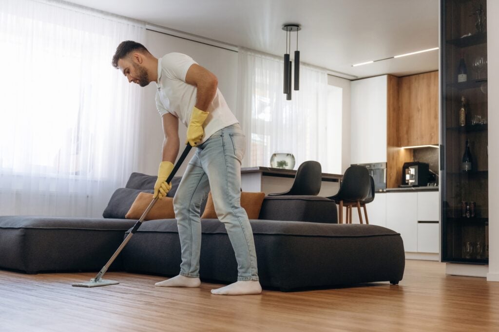 Man mopping hardwood floor with yellow gloves. Residential cleaning services in Washington DC, keeping your home spotless.